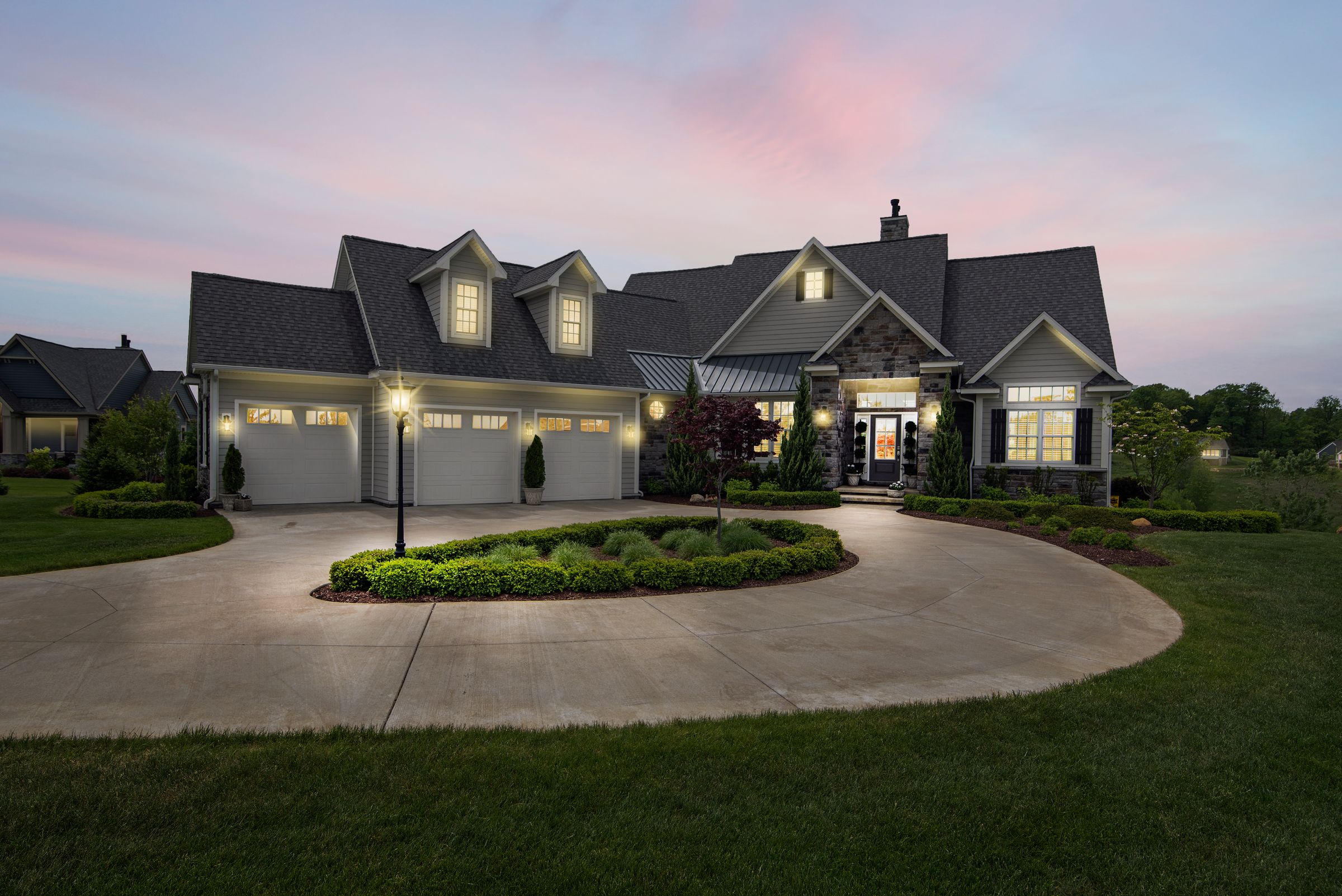 A suburban home at dusk with its exterior and window lights on.
